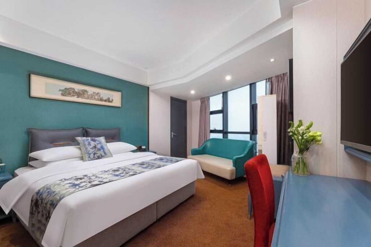 A hotel room with a bed, a desk, a chair, a TV, and a window with curtains.