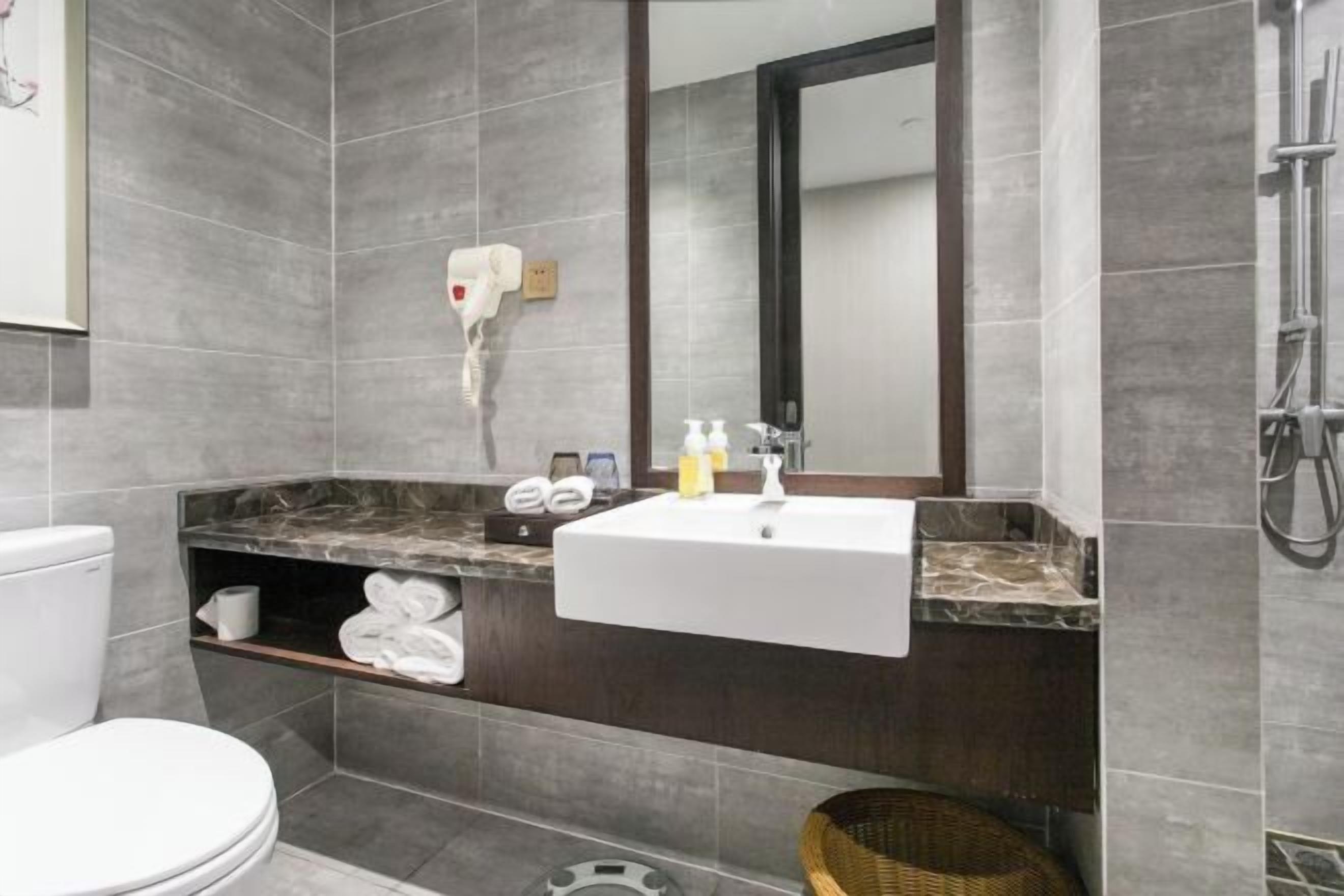 A modern bathroom with a white sink, dark marble countertop, and a large mirror.