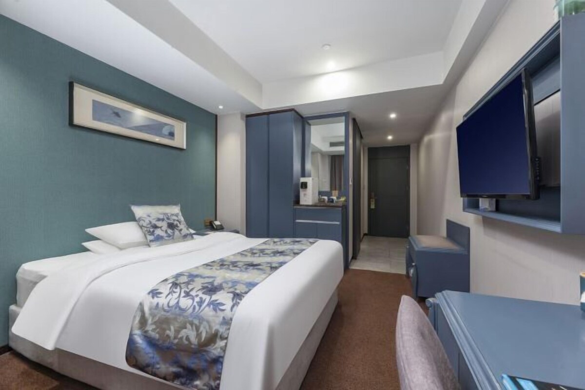 A hotel room with a bed, a desk, a television, and a bathroom visible through an open door.