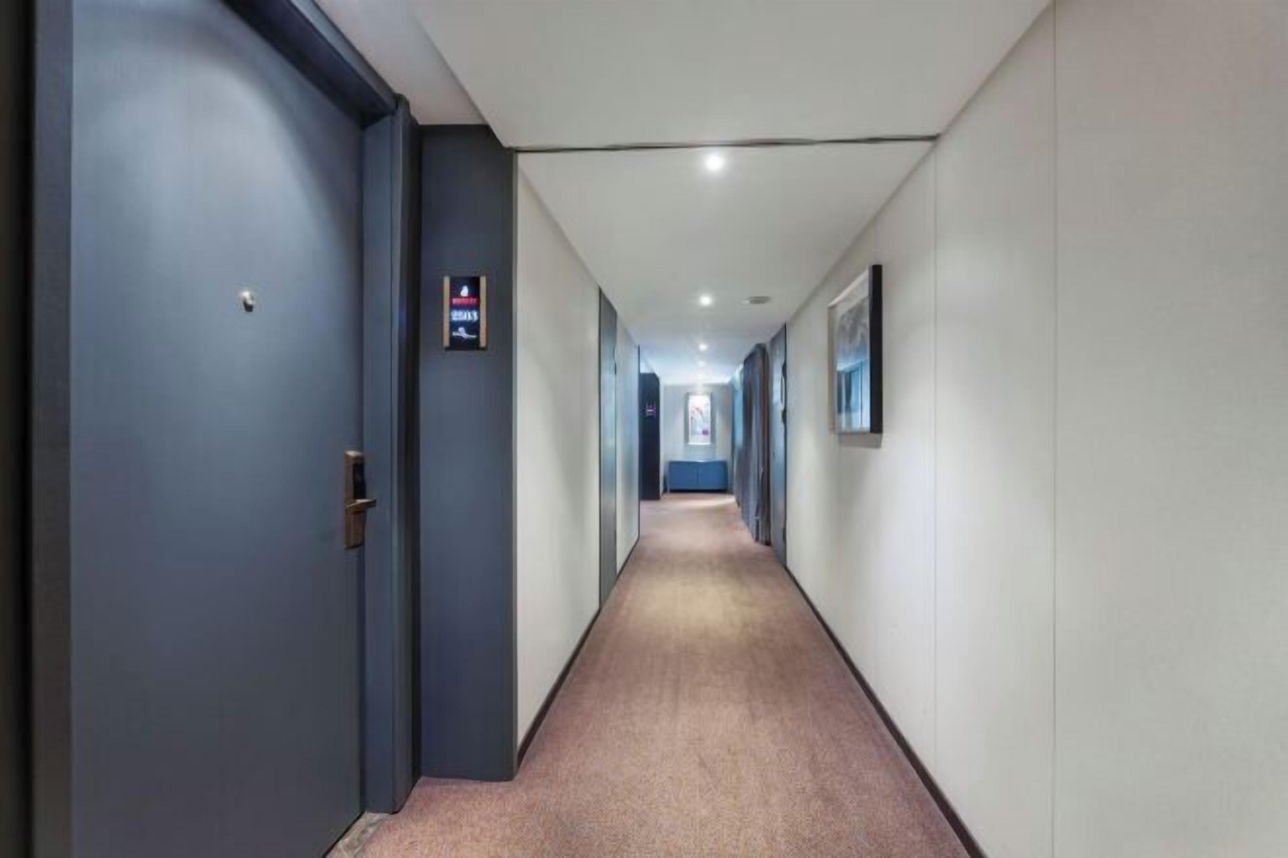 Un pasillo largo y estrecho con piso alfombrado, una puerta a la izquierda y un cartel en la pared.