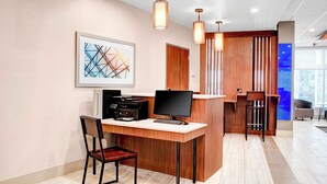 A modern office space with a desk, computer, printer, and a chair. There is a framed abstract artwork on the wall and a reception area with a counter and stools. - Holiday Inn Express & Suites Coldwater by IHG (Coldwater)