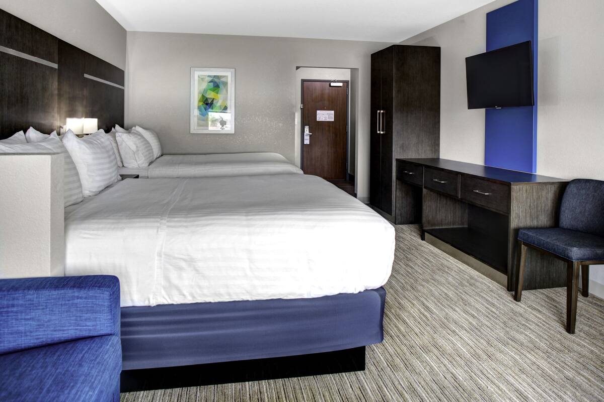 Ein Hotelzimmer mit einem großen Bett, einem Schreibtisch mit Schubladen, einem Stuhl, einem flachbildfernseher an der Wand und einer Tür mit einem Schild.
