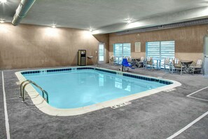 An indoor swimming pool with a clear blue water, surrounded by a grey floor and walls, with a seating area and a door to the right. - Holiday Inn Express & Suites Coldwater by IHG (Coldwater)