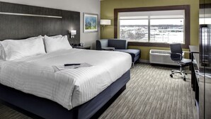 A hotel room with a large bed, a desk with a chair, a window with a view, and a wall-mounted heater. - Holiday Inn Express & Suites Coldwater by IHG (Coldwater)