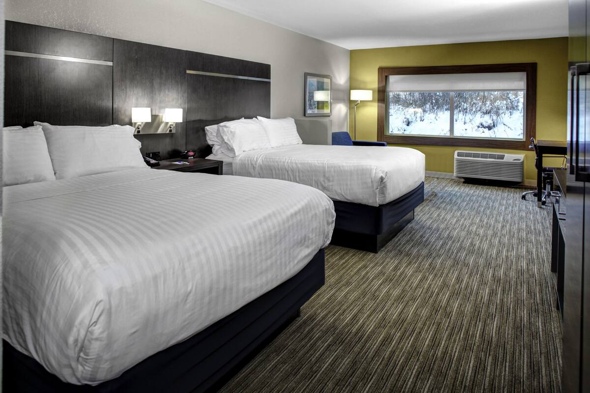 Ein Hotelzimmer mit zwei Betten, einem großen Fenster mit Blick auf eine verschneite Landschaft, einem Schreibtisch mit Lampe und einer Wand-Klimaanlage.