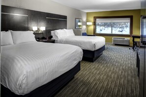 Une chambre d’hôtel avec deux lits, une grande fenêtre donnant sur un paysage enneigé, un bureau avec une lampe et un climatiseur fixé au mur.
