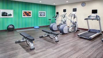 Ein Fitnessraum mit Laufbändern, Crosstrainern und einer Bank.