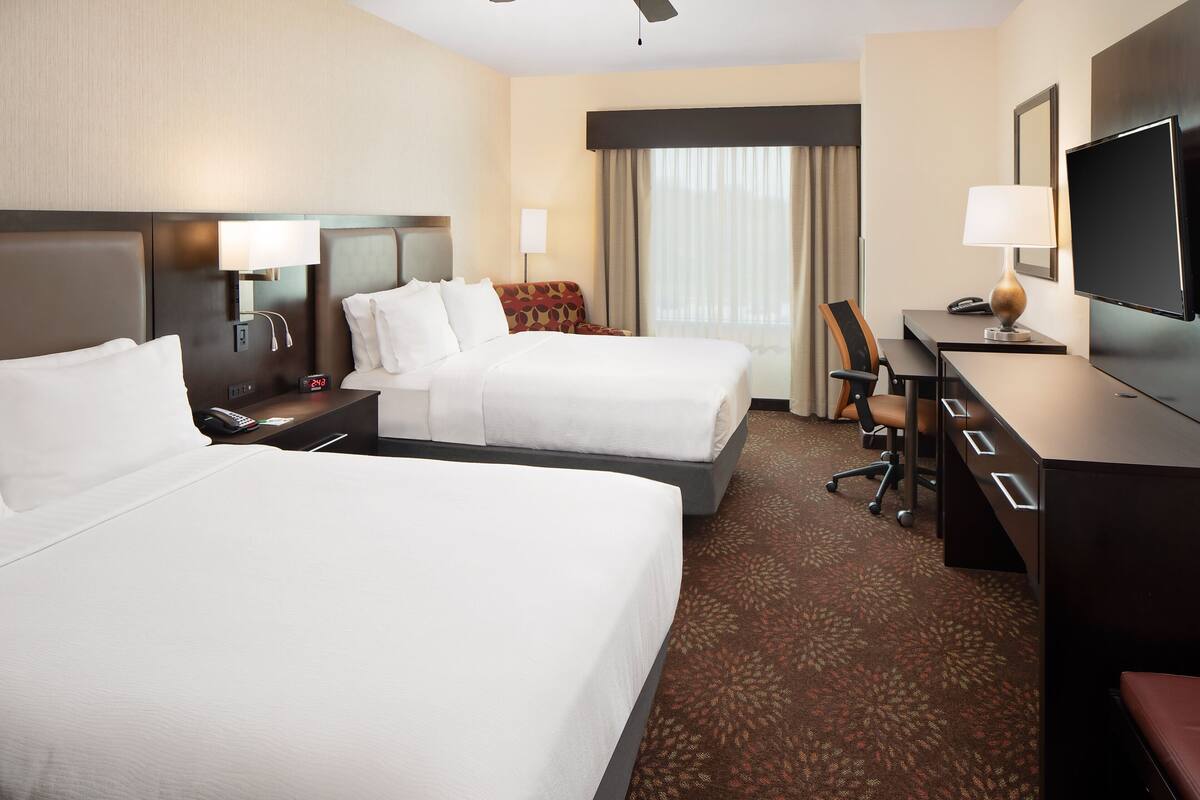 A hotel room with two beds, a desk with a chair, a TV, and a lamp.