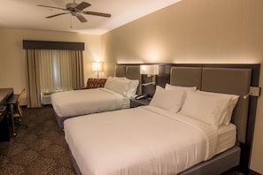 Ein Hotelzimmer mit zwei Betten, einem Schreibtisch, einem Stuhl, einem Deckenventilator und einem Vorhangfenster.
