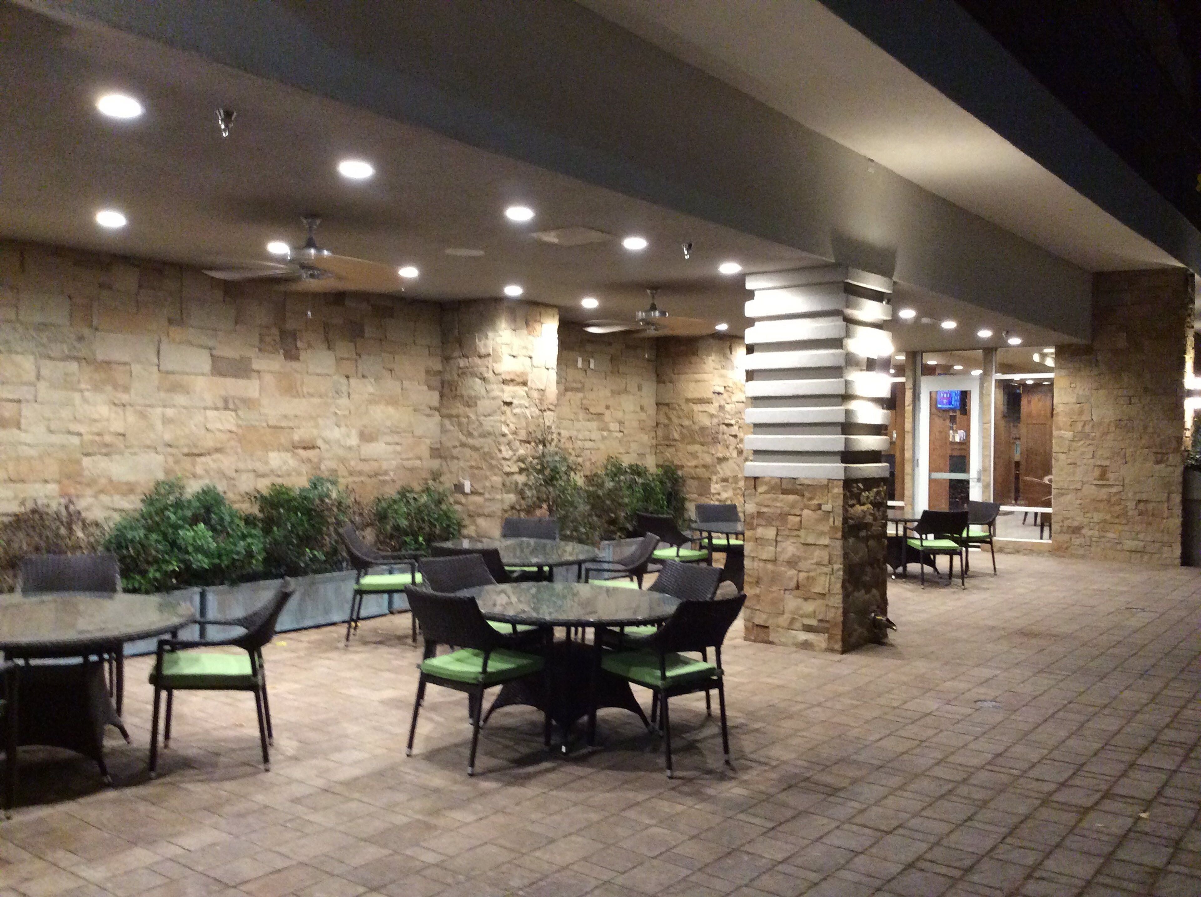 An outdoor patio area with stone walls, multiple tables and chairs, and ceiling lights.
