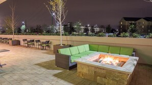 An outdoor seating area with a fire pit, green cushioned sofa, and chairs. - Holiday Inn Trophy Club by IHG (Roanoke)