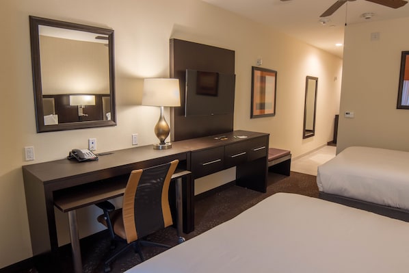 Ein Hotelzimmer mit Schreibtisch, Stuhl, zwei Betten, einem Spiegel und einer Lampe.