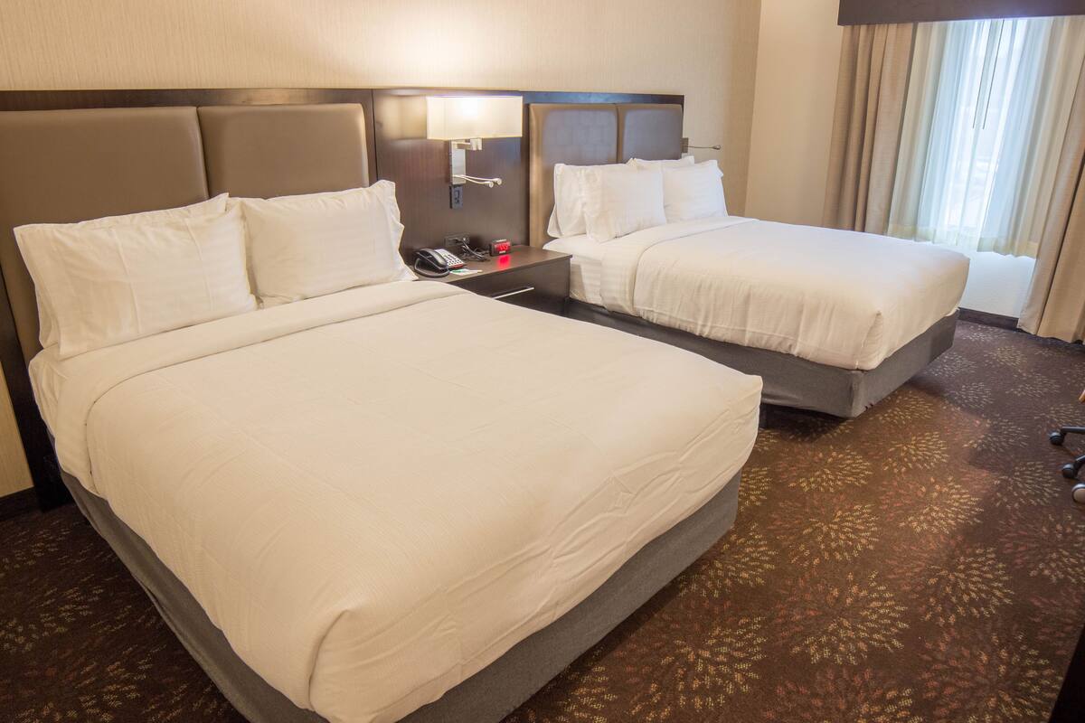 A hotel room with two beds, a nightstand with a lamp, and a telephone.