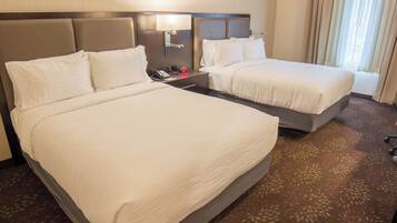 A hotel room with two beds, a nightstand with a phone and a lamp, and a carpeted floor.