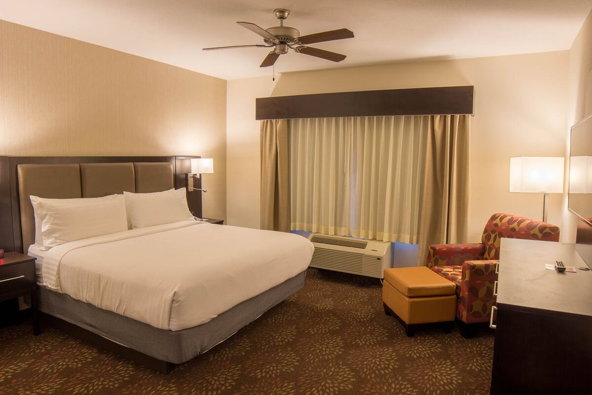 A hotel room with a large bed, a desk, a chair, a ceiling fan, and a window with curtains.