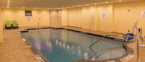 Una piscina interior con un cartel de prohibición de saltos, una silla de socorrista y un elevador para piscina.