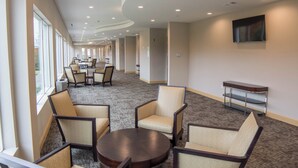 A hotel lobby with a long corridor, seating area with chairs and tables, and a flat-screen TV mounted on the wall. - Holiday Inn Trophy Club by IHG (Roanoke)