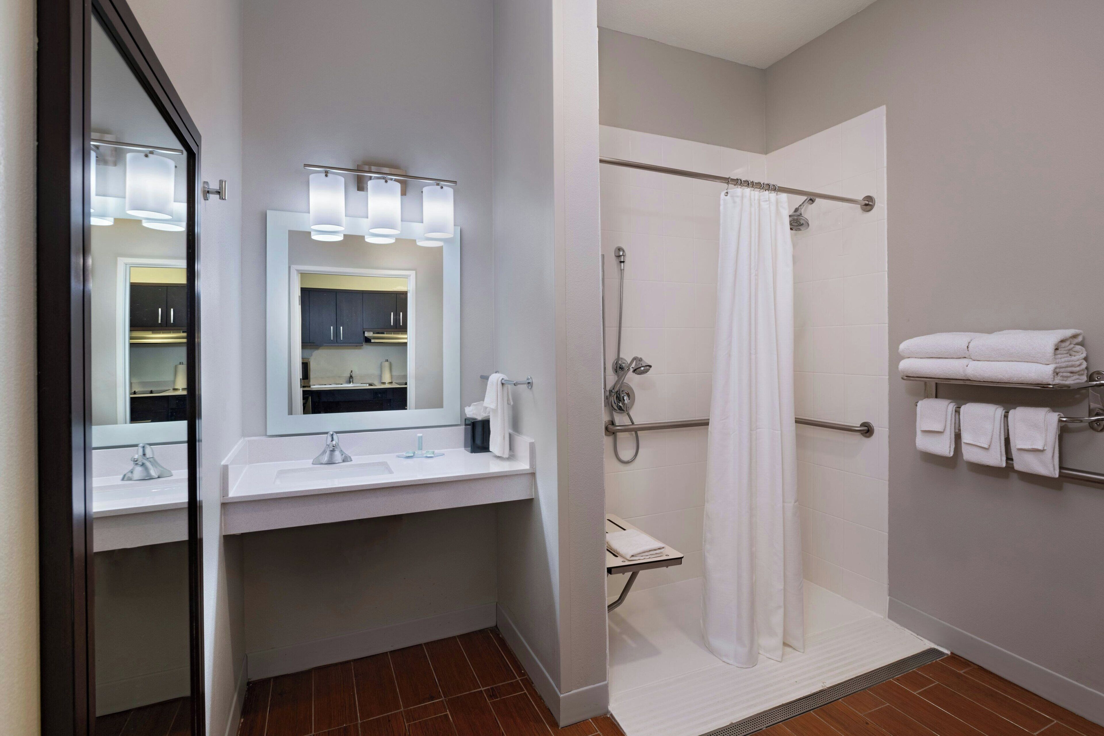 A modern bathroom with a double sink, a shower with a glass door, and a towel rack with folded towels.