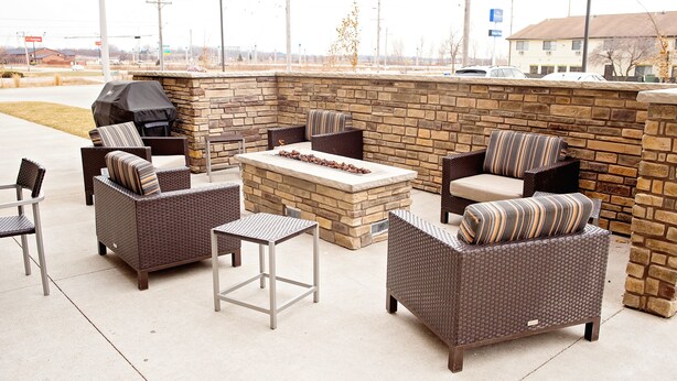 An outdoor patio area with wicker furniture, a stone fireplace, and a grill. - TownePlace Suites by Marriott Ames (Ames)