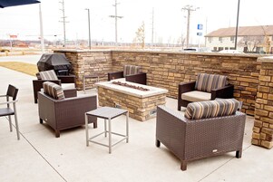 Un patio al aire libre con mobiliario de mimbre, chimenea de piedra y una parrilla.