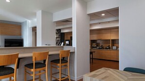 A modern kitchen with wooden cabinets, a built-in stove, and a bar area with stools. - TownePlace Suites by Marriott Ames (Ames)