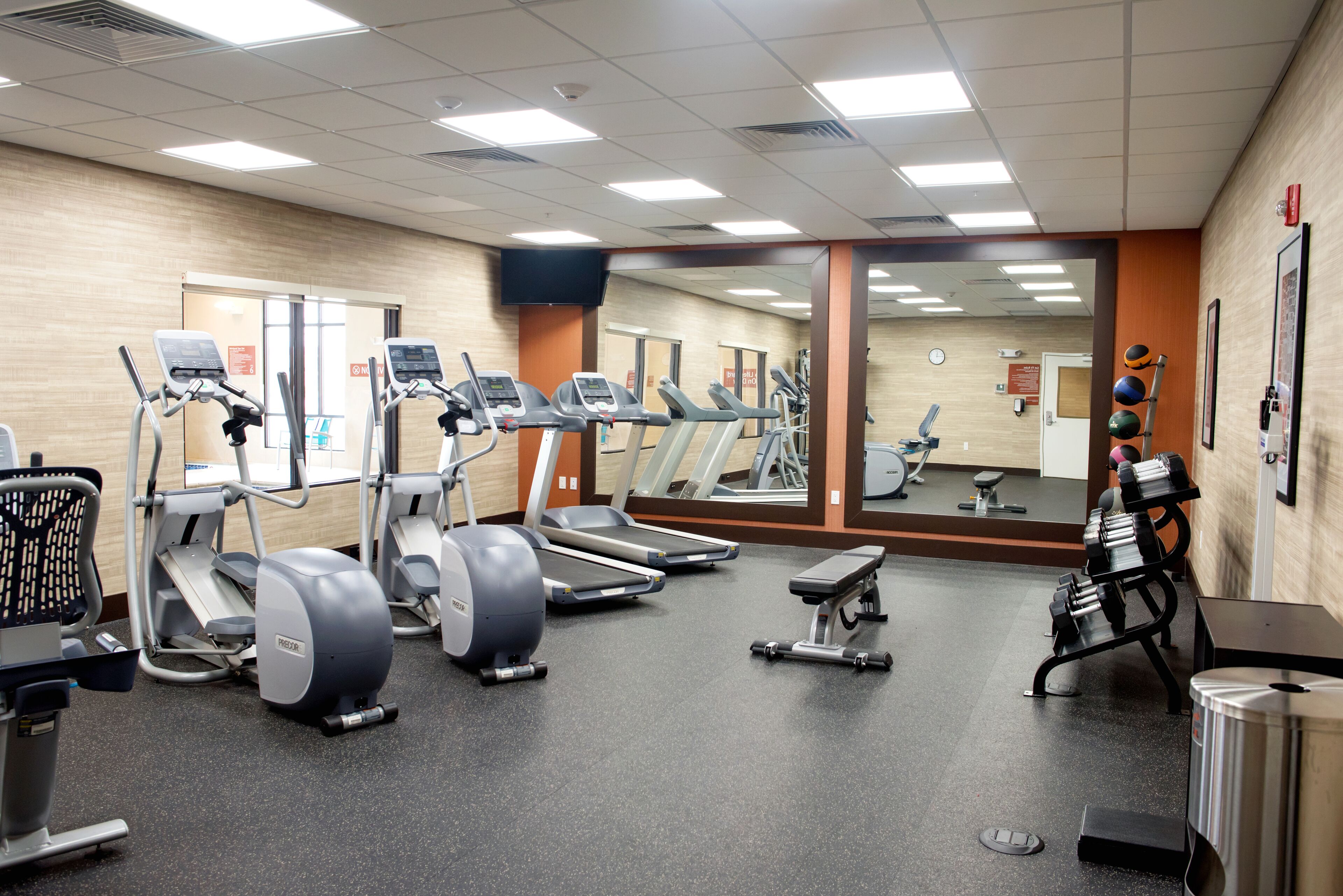 Un gimnasio con cintas de correr, elípticas y un muro de espejos.