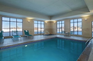 Una piscina interior con ventanas transparentes, sillas y vistas al exterior.