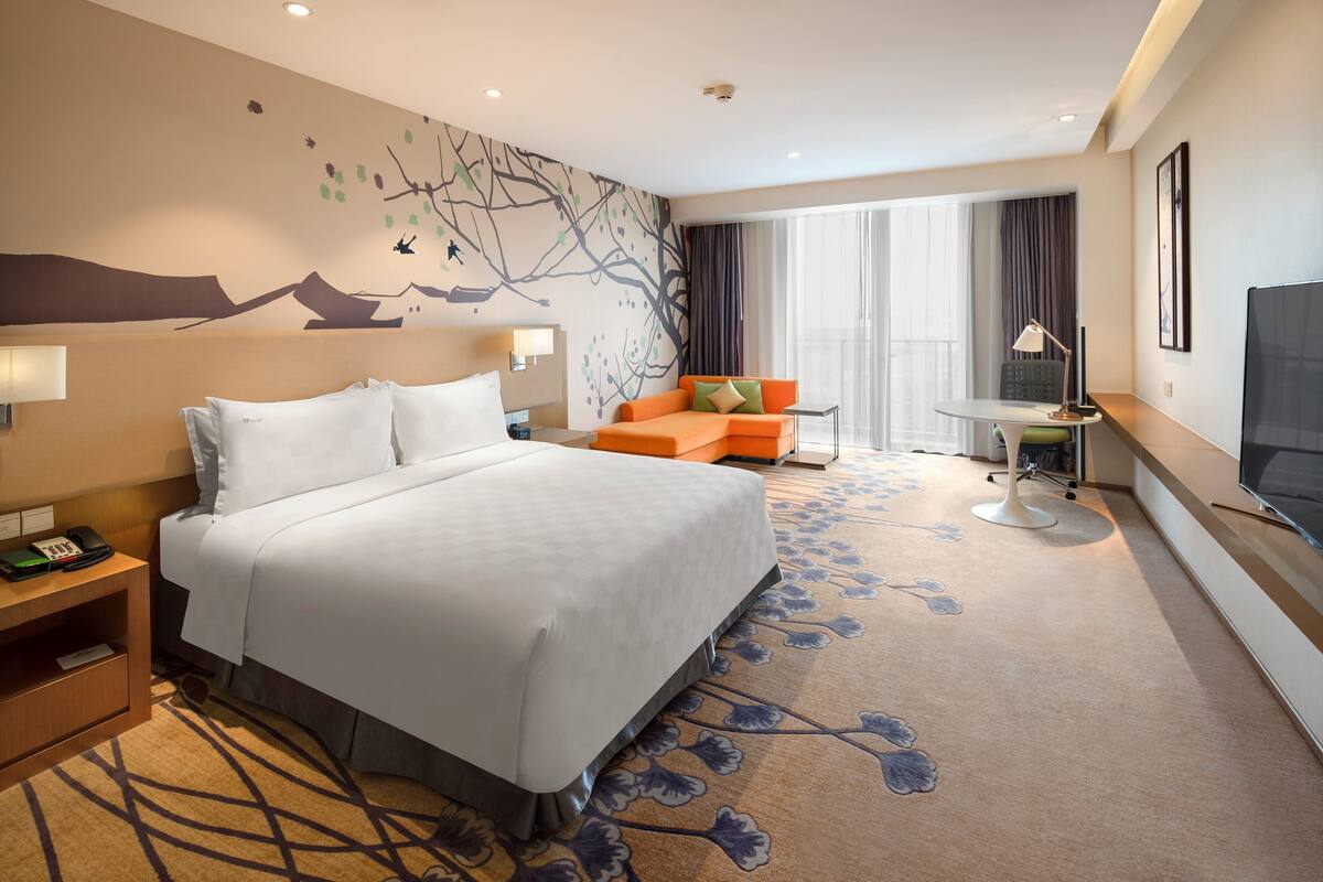 A hotel room with a large bed, a sofa, a small table, and a TV.