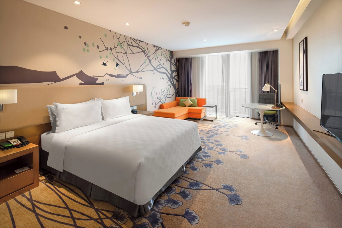 A hotel room with a large bed, a sofa, a small table, and a TV.