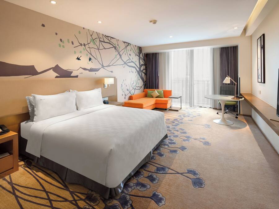 Ein Hotelzimmer mit einem großen Bett, einem Schreibtisch mit Lampe, einer Couch und einem Fernseher.