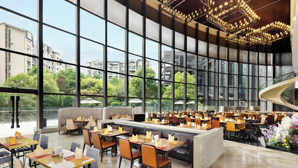 A spacious restaurant with large windows offering views of buildings and greenery.