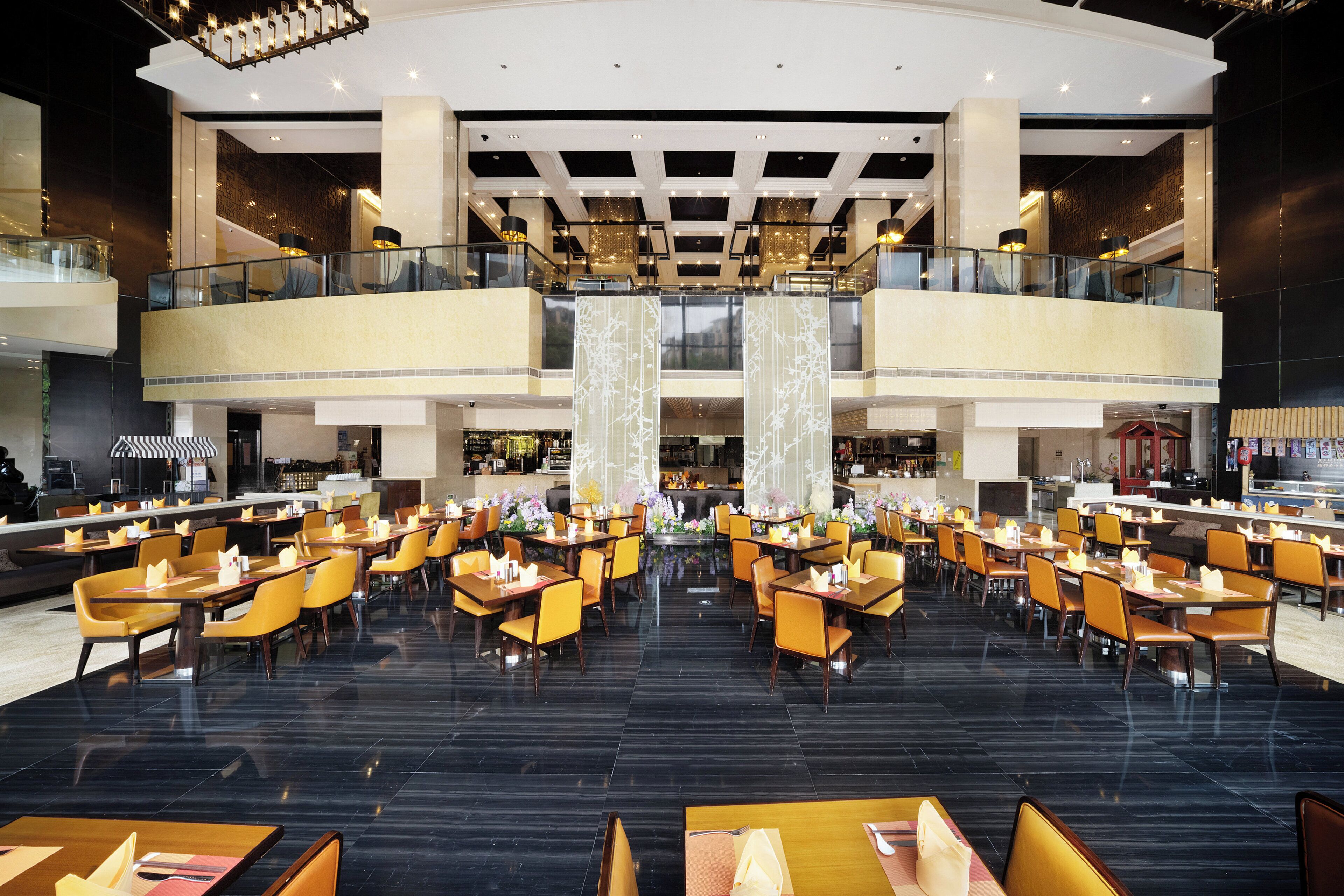 A spacious hotel lobby with multiple dining areas, a central atrium, and a second-floor balcony.