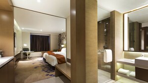 A modern hotel room with a large bed, a desk, a shower area, and a bathroom with a mirror and sink.