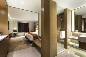 Une chambre d’hôtel moderne dotée d’un grand lit, d’un bureau, d’un espace douche et d’une salle de bain avec un miroir et un lavabo.