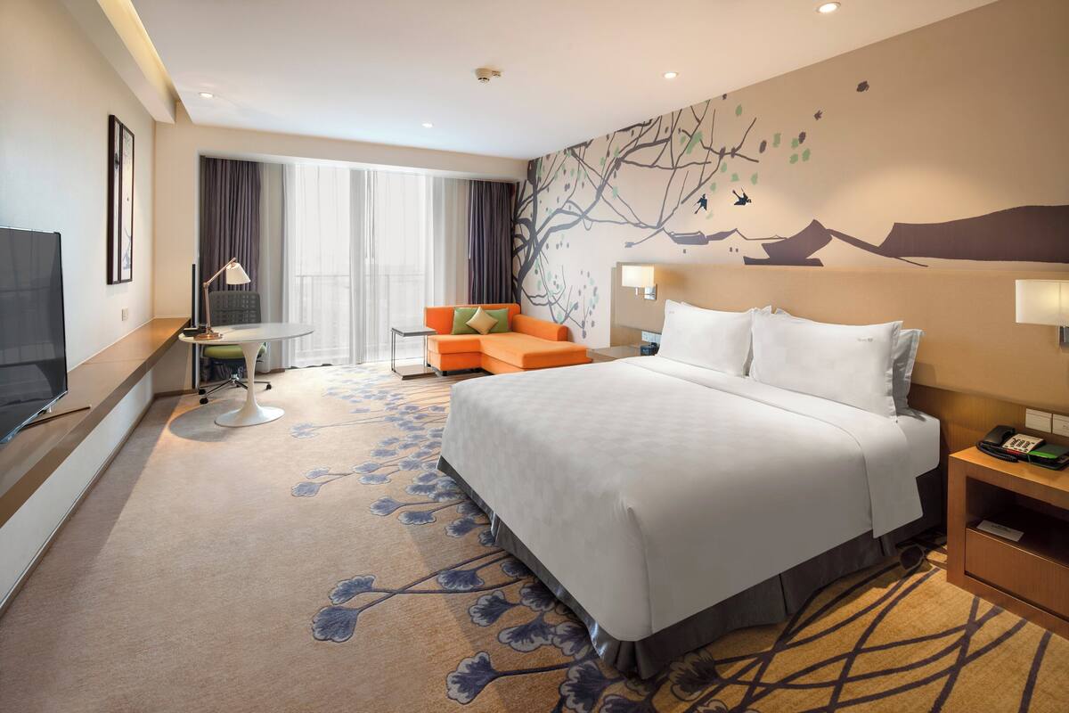 A hotel room with a large bed, a sofa, a desk, and a TV.