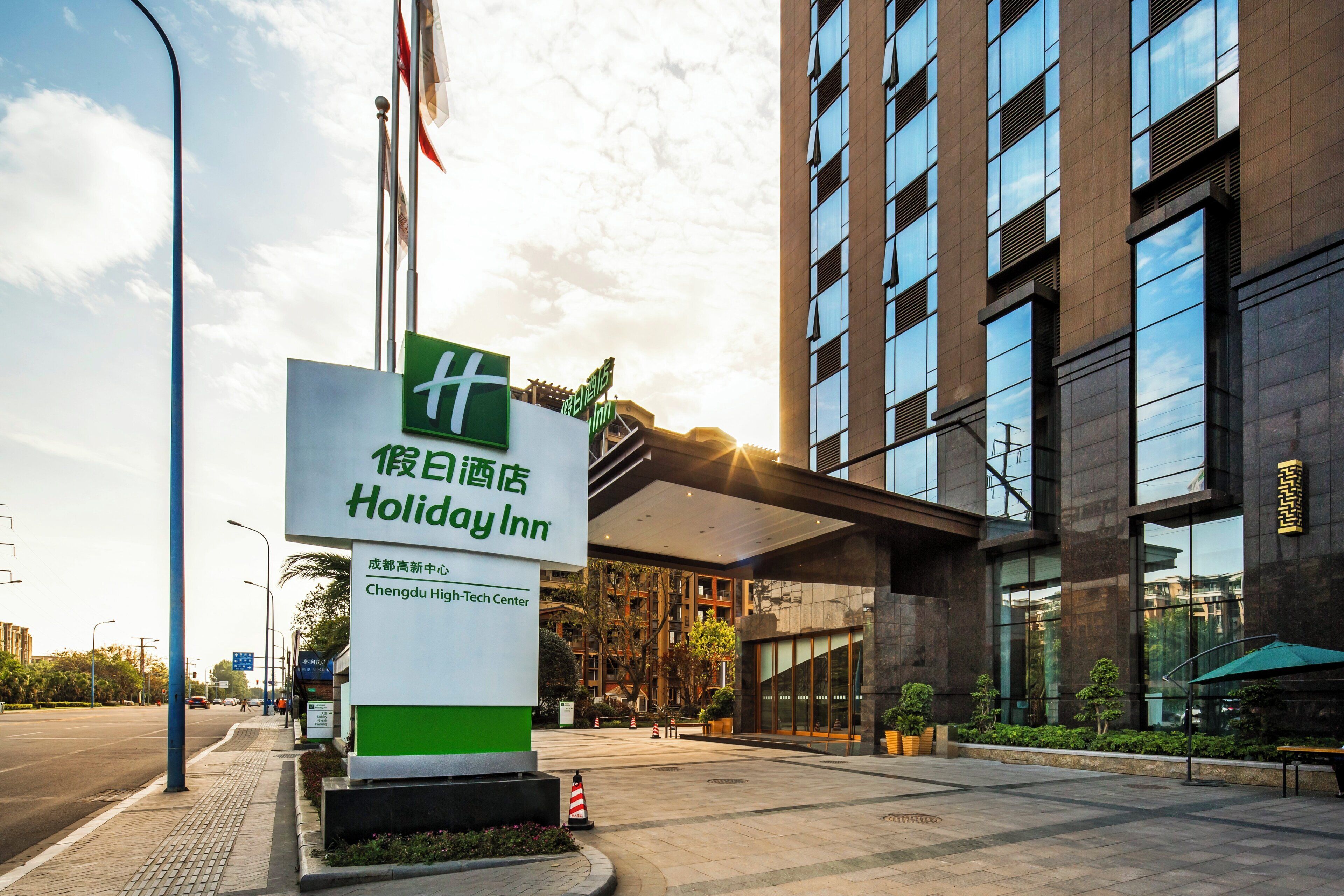 A Holiday Inn sign with a green and white color scheme, located in front of a modern building with a glass facade.