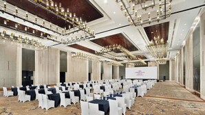 A large conference room with rows of tables and chairs, a stage with a screen, and multiple chandeliers.