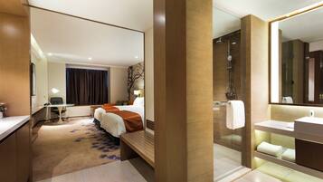 A hotel room with a bed, a desk, a chair, a shower, and a bathroom.