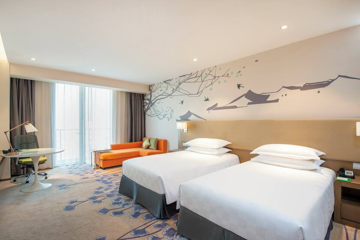 A hotel room with two beds, a desk, a chair, and a sofa.