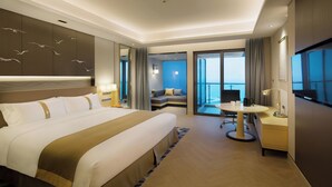 Une chambre d’hôtel avec un grand lit, un bureau avec une chaise, une petite table, une télévision et un balcon avec vue.