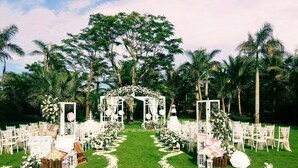 Un lieu de réception en plein air pour les mariages, agrémenté d’une arche blanche, de chaises blanches et de décorations florales.