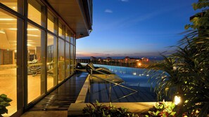 A swimming pool with a glass barrier, a view of the sea, and a building with large windows. - Holiday Inn Haikou West Coast by IHG (Haikou)