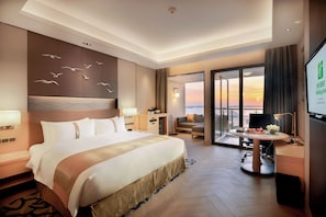 A hotel room with a large bed, a desk, a chair, a TV, and a balcony with a view. - Holiday Inn Haikou West Coast by IHG (Haikou)