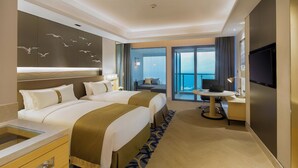Une chambre d’hôtel avec deux lits, un bureau avec un ordinateur portable, une télévision et un balcon avec vue sur la mer.