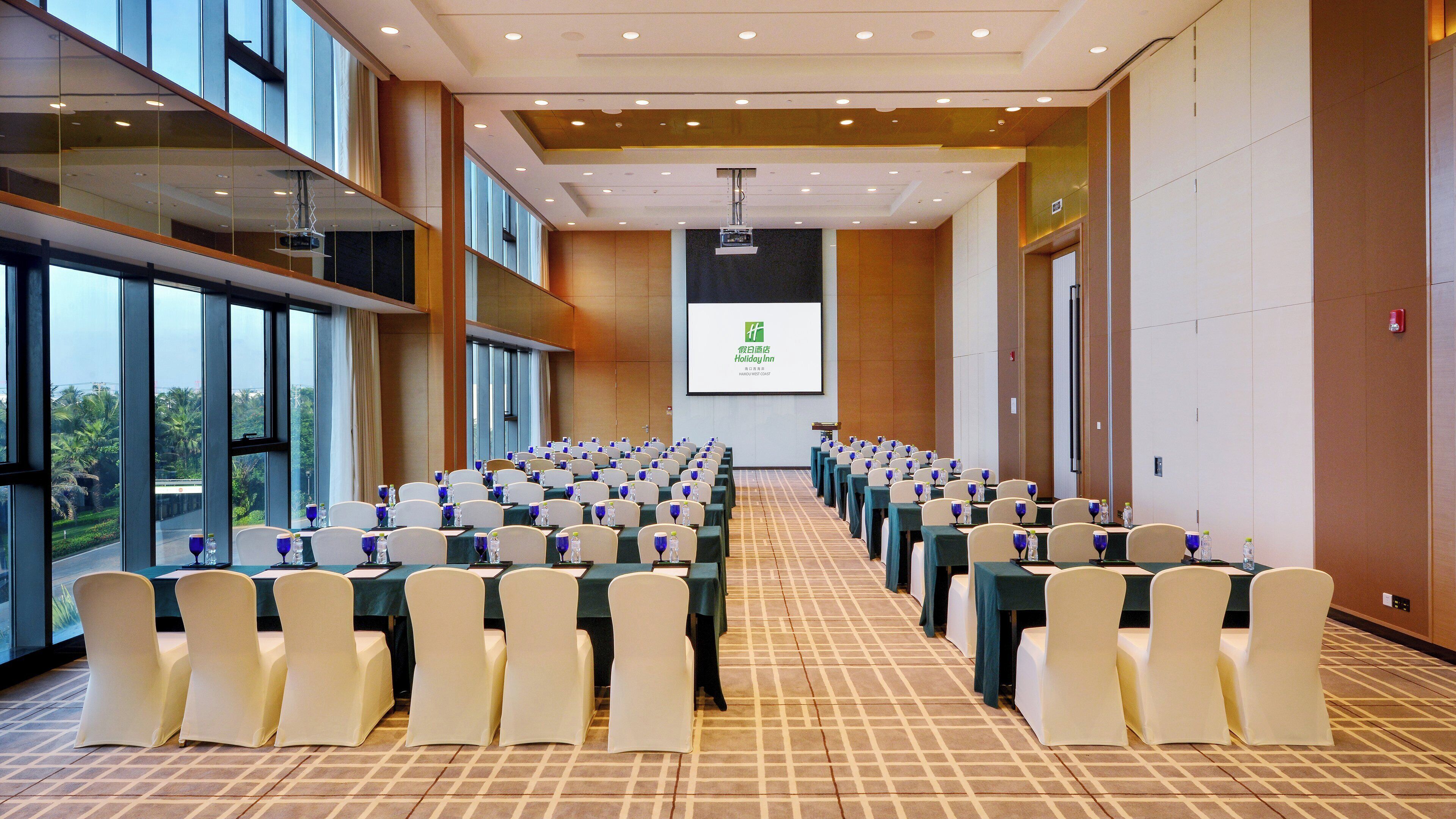 A conference room with rows of tables and chairs, large windows, and a projection screen.