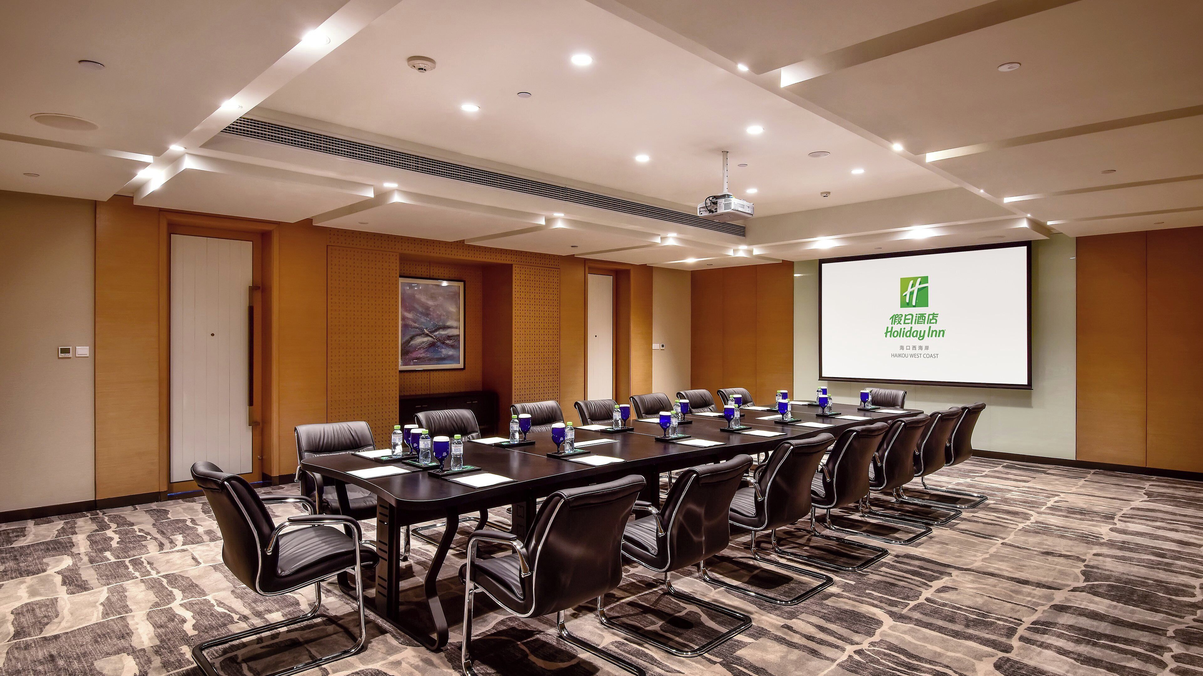 A conference room with a long table, chairs, a projector screen, and a carpeted floor.