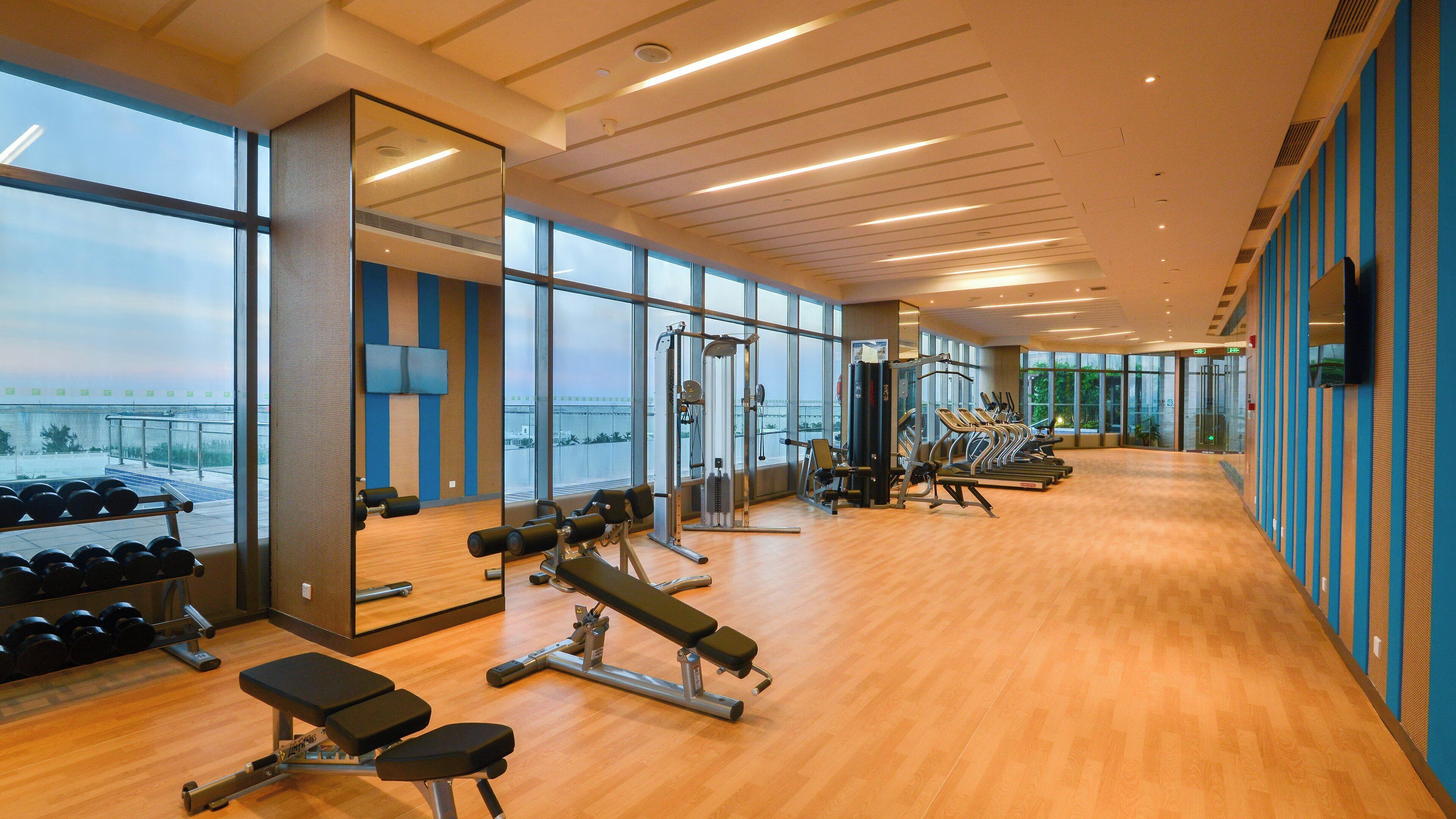 A gym with exercise equipment, large windows, and a view of the outside.
