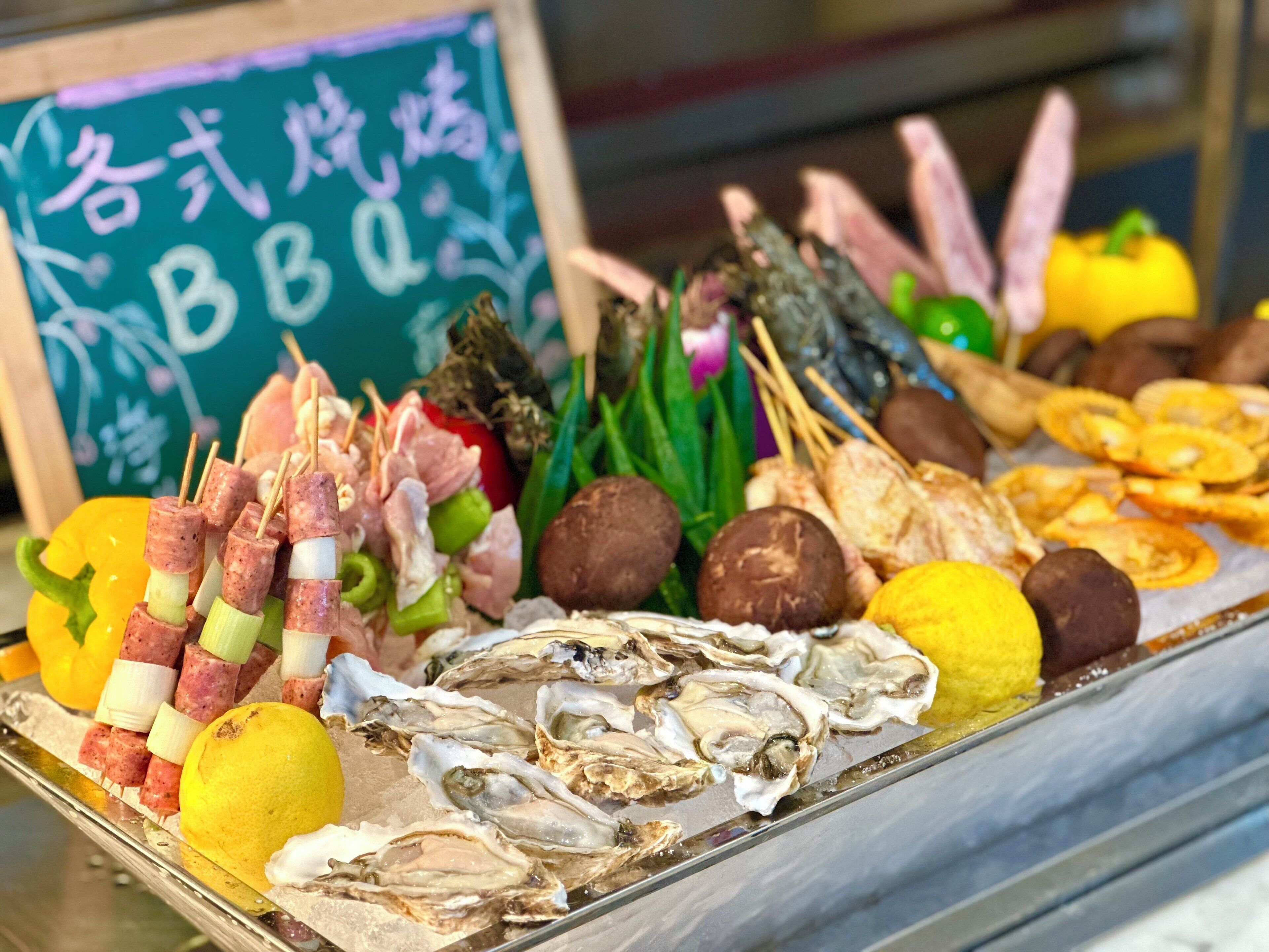 A variety of seafood and vegetables on a tray, including oysters, lemon slices, and skewered meat.