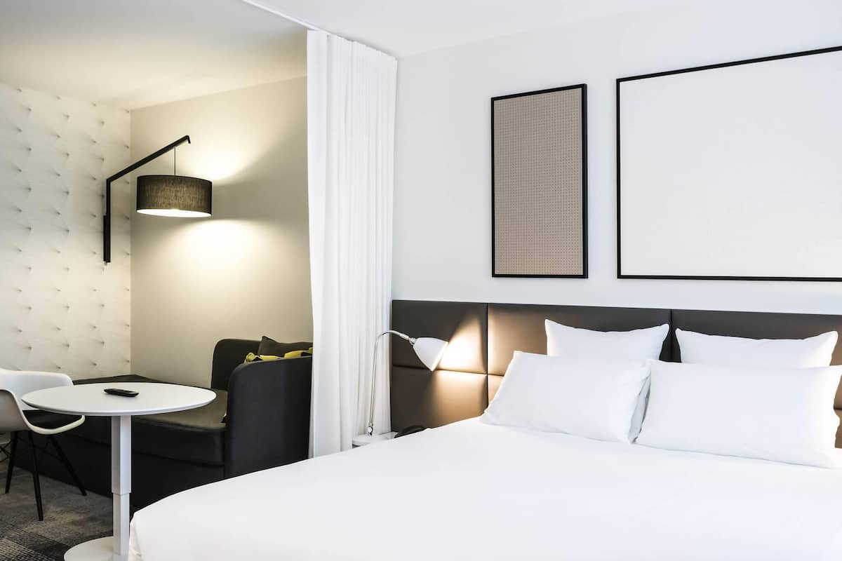 A hotel room with a bed, a desk, a chair, and a lamp.