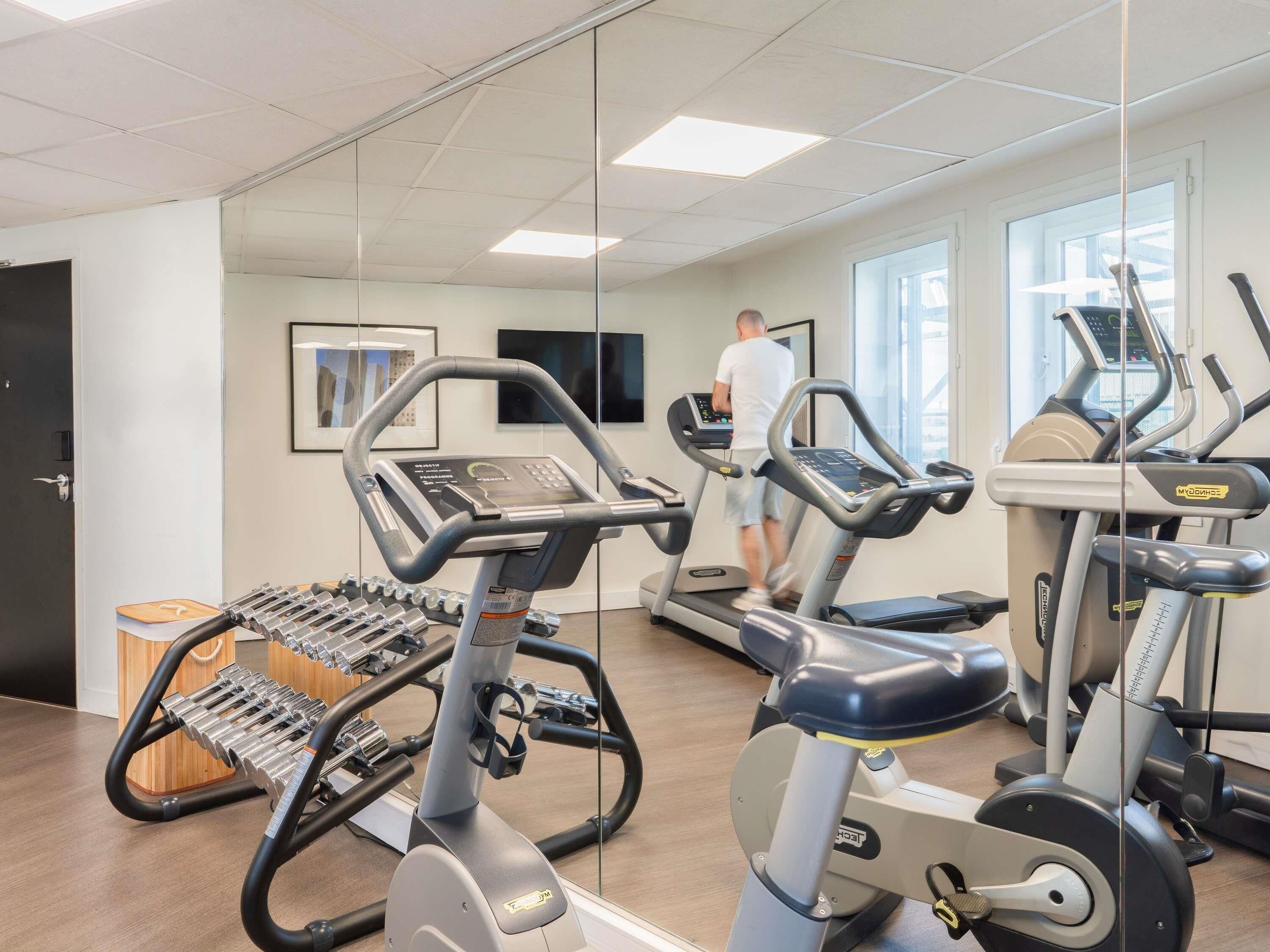 Une salle de sport équipée de tapis de course, de vélos elliptiques et d’appareils de musculation.